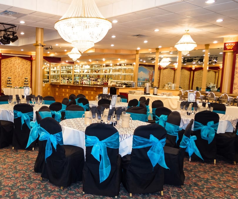 Elegant banquet hall with black chairs, turquoise bows, zebra-print tables, and a full bar.