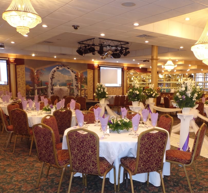 A large banquet hall with round tables set with white tablecloths, purple napkins, and floral centerpieces.