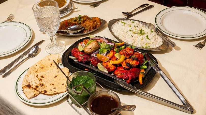 A table laden with Indian dishes, including tandoori chicken, rice, curry, naan, and sauces.