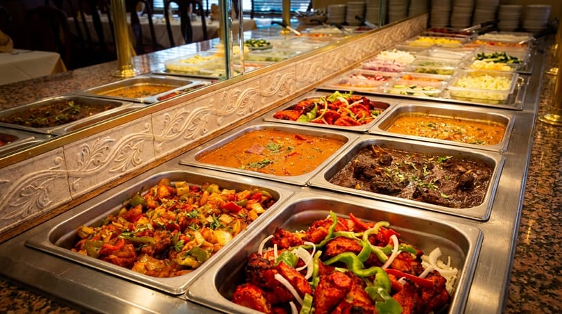 A buffet line filled with various Indian dishes in metal serving trays.