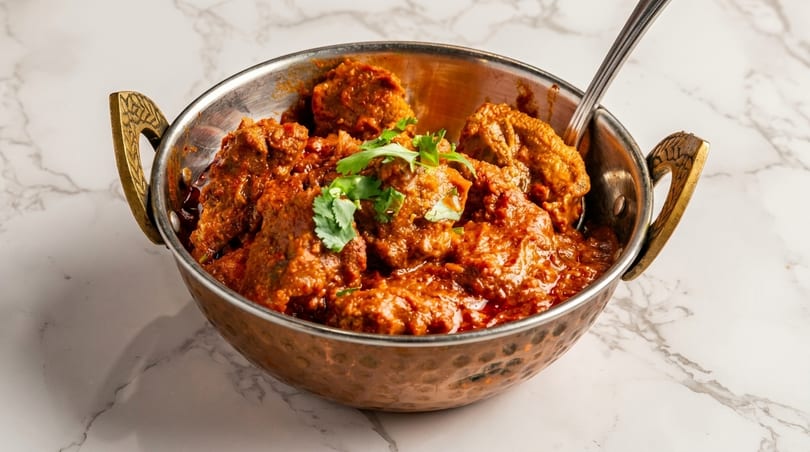 Copper bowl filled with rich, red curry, garnished with fresh cilantro, on a marble surface.