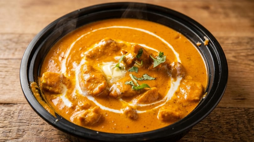 Steaming butter chicken curry in a black bowl, garnished with cream swirls and fresh cilantro.